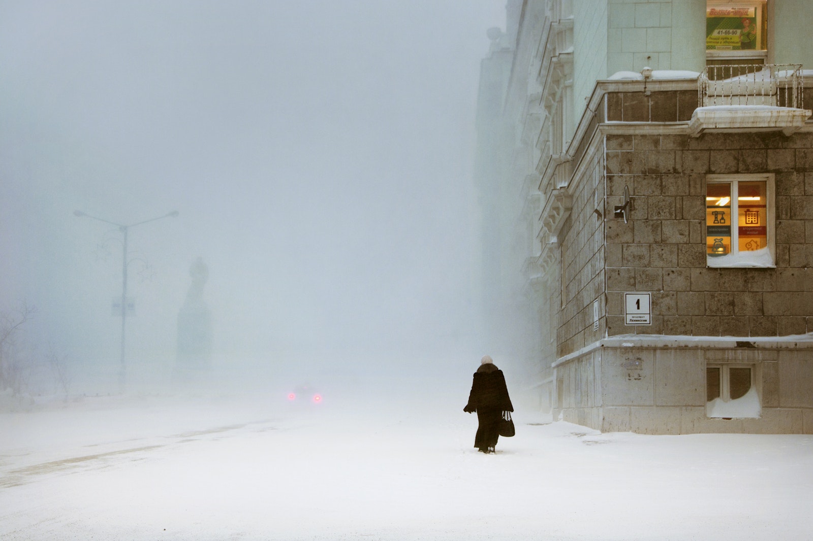 Person walking in a snowy street with a building in the background
