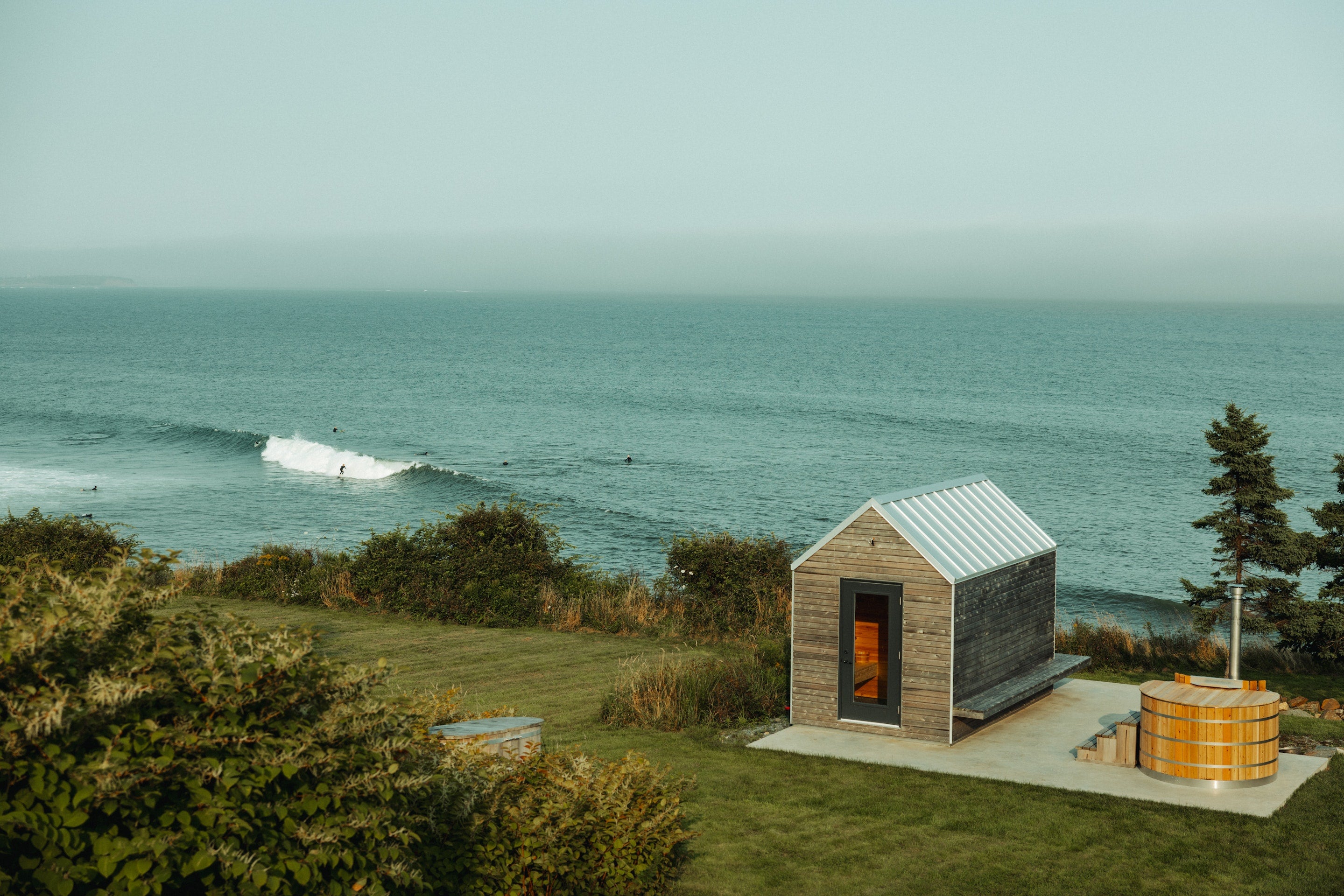 Small wooden cabin by the ocean with a hot tub.
