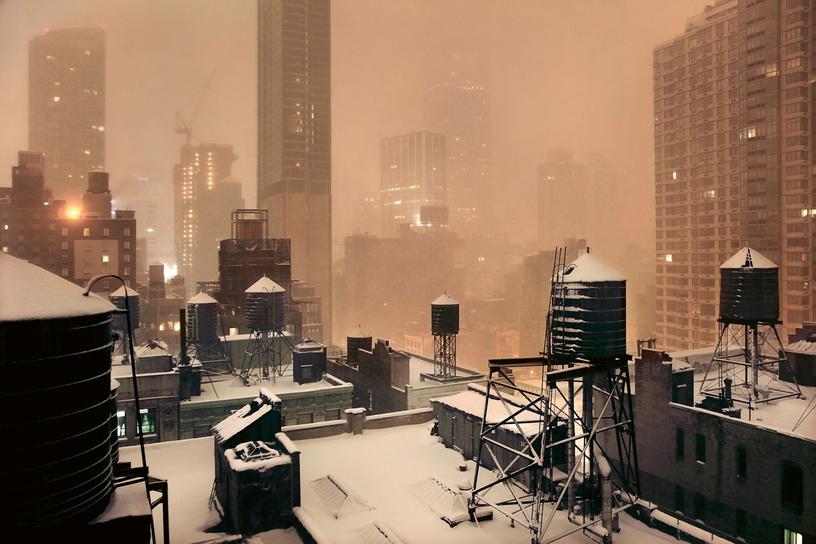 Cityscape with snow-covered rooftops and tall buildings during a snowstorm.