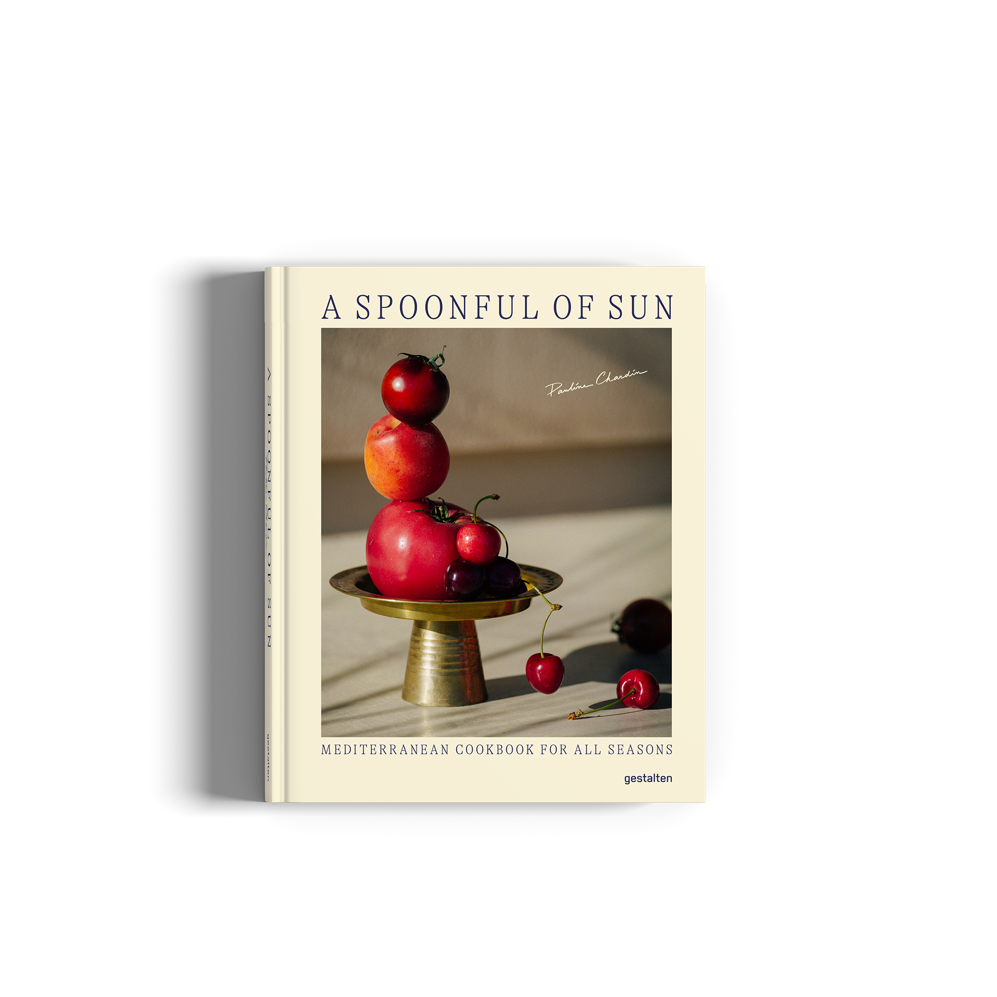 A Spoonful of Sun: Mediterranean Cookbook for All Seasons shows as a cream-colored cover and a still life photograph of red apples and cherries on a pedestal.