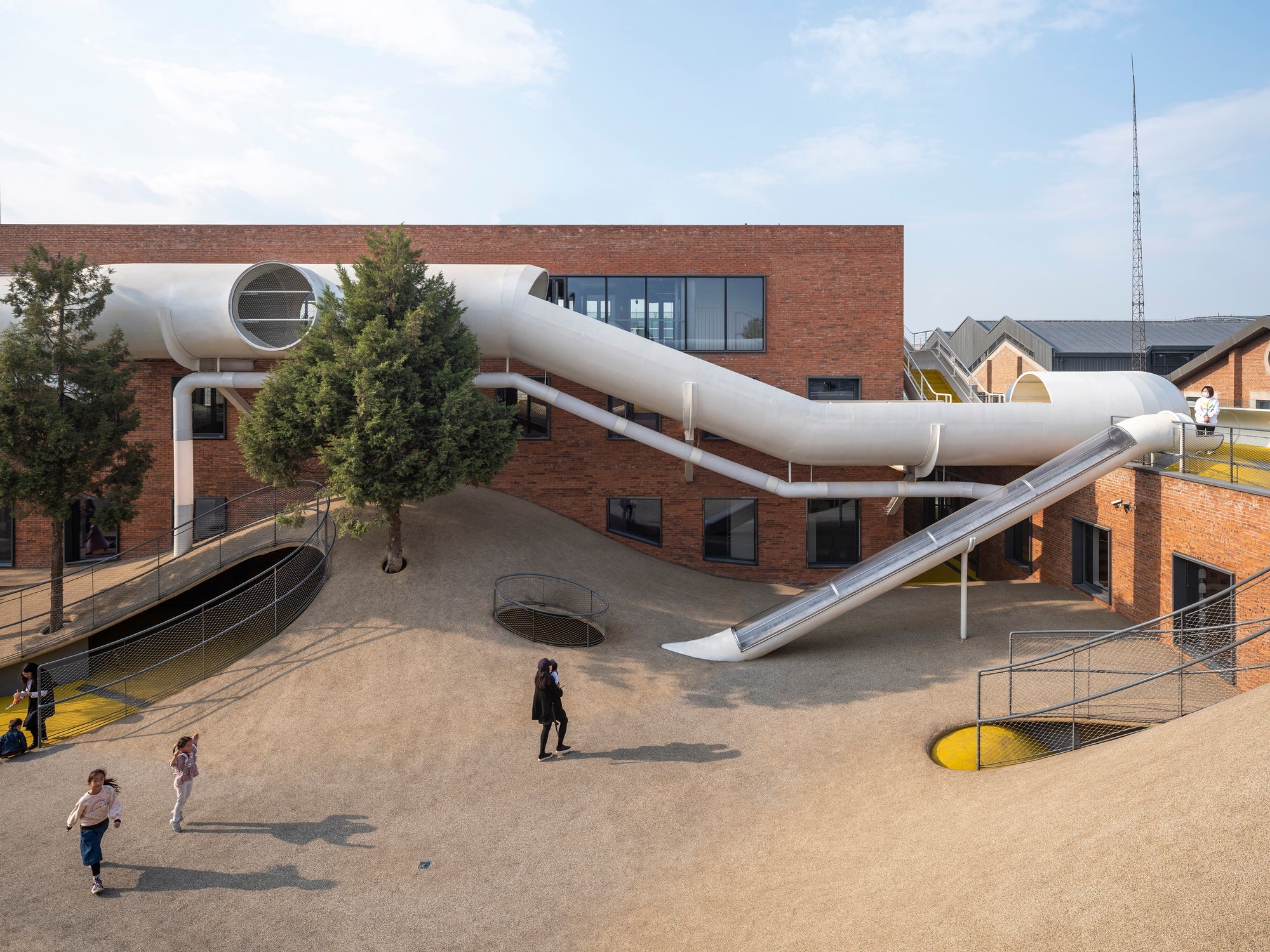 When designers We Architech Anonymous (WAA) began transforming The Playscape from warehouses into a children’s community center, they immediately encoun- tered problems. In the site’s courtyard were several illegal residences, which had resulted in local authorities placing legislative restrictions on its development. These rulings protected the existing trees and prohibited changes to the massing, layout, materials, and fenestration of the buildings.