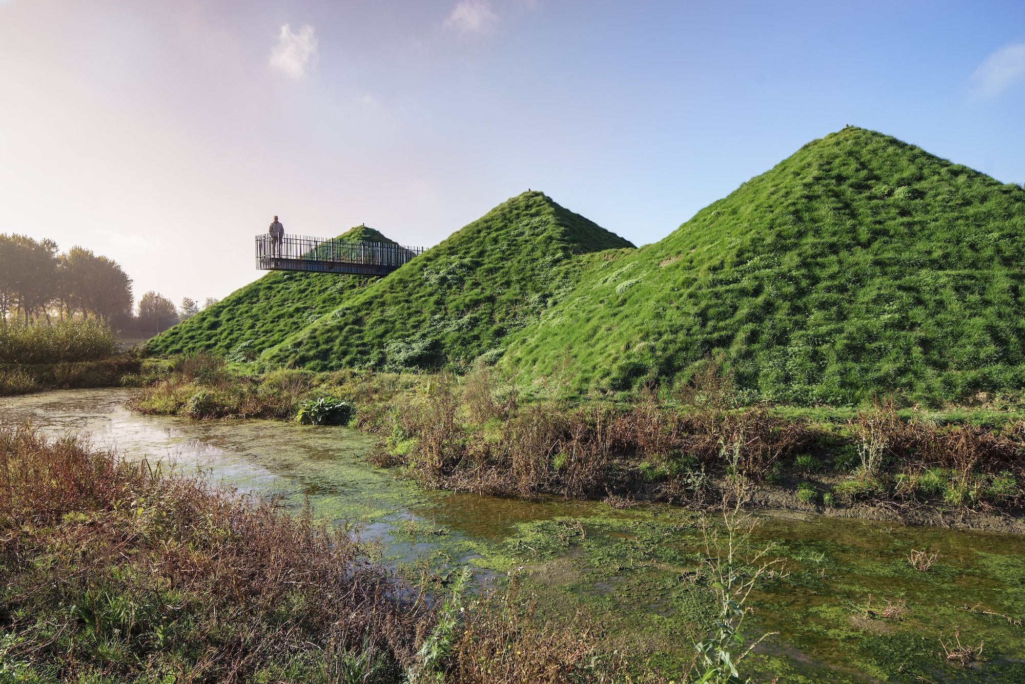 Located on a man-made island in the wetlands of the De Biesbosch National Park, Studio Marco Vermeulen has transformed this local museum: adding a 11,000-square-foot (1,000-square-meter) wing, immersive roofscape, and freshwater tidal park. A green roof blankets the scheme, with a weaving walkway that encourages visitors to explore the terrain. The new wing incorporates generous expanses of floor-to-ceiling, heat-resistant windows, looking out onto the marshland surroundings.